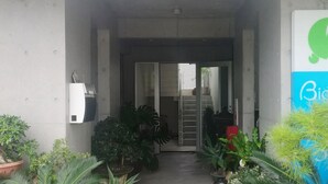 A building entrance with a green turtle logo, a door, and potted plants. - Room Biotop YOMITAN (Yomitan)