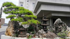 A modern building with a landscaped garden featuring a pine tree, a traditional lantern, and rock formations. - Room Biotop YOMITAN (Yomitan)