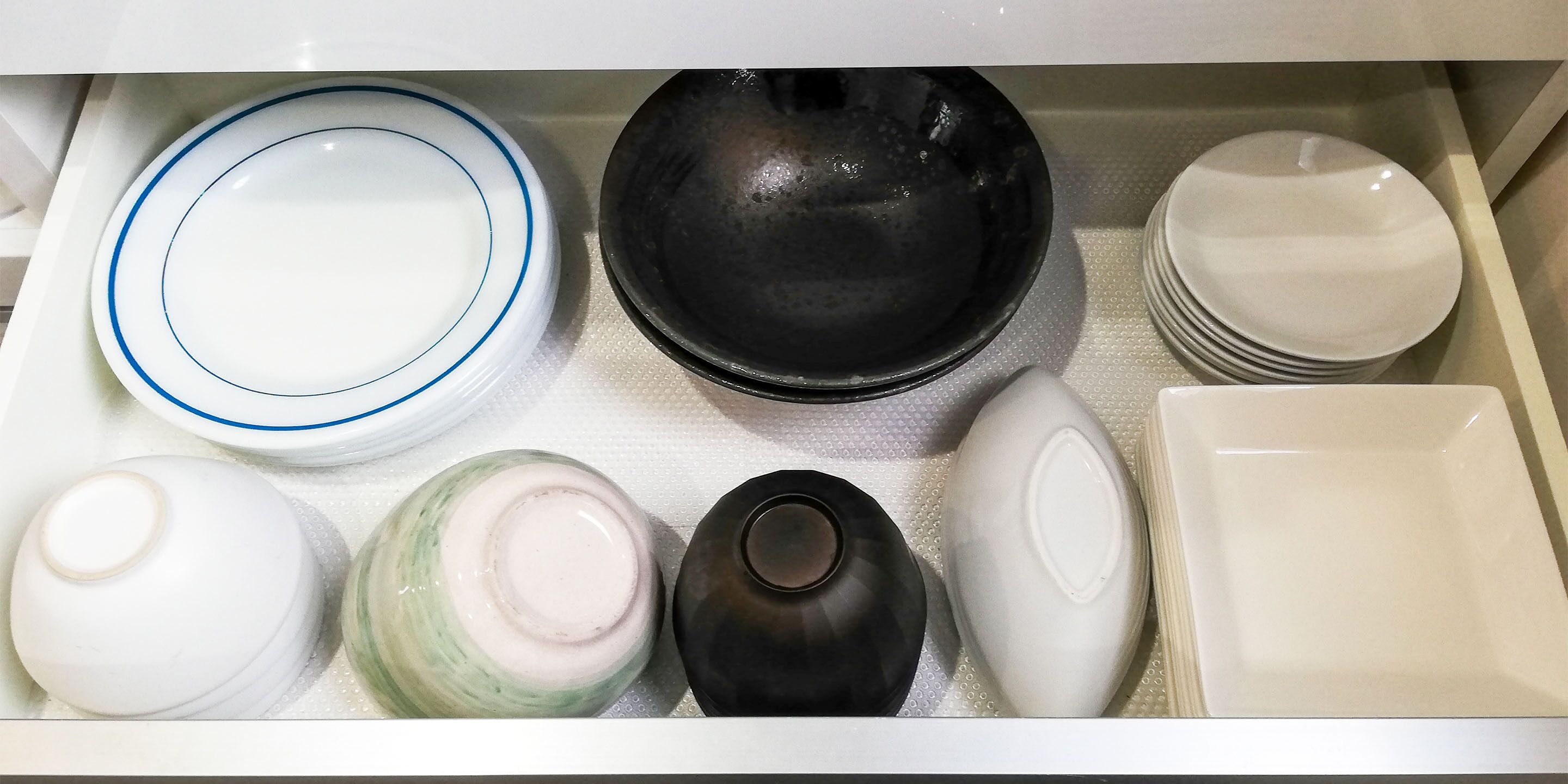 A drawer containing various kitchenware items including plates, bowls, and jars.