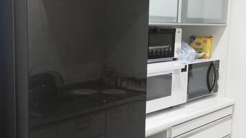 A kitchen with a microwave, a stove, and a shelf with a bag of chips.