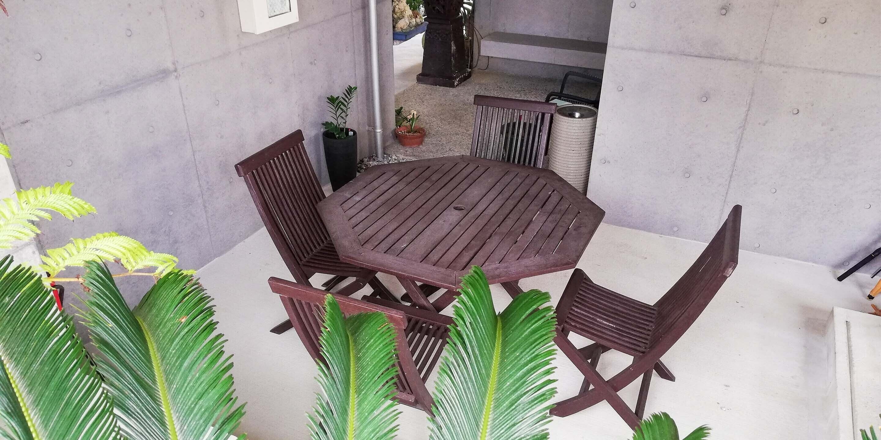 Ein Patio mit einem runden Holztisch und vier Holzstühlen. Blumentöpfe und ein Mülleimer sind sichtbar.