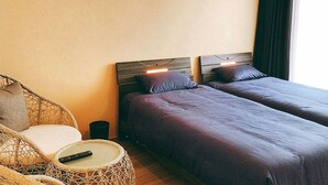 A hotel room with two beds, a wicker chair, a small round table, and a remote control on the table. - Room Biotop YOMITAN (Yomitan)