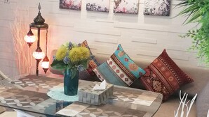 A glass-top table with a patterned table runner, a vase with yellow flowers, and a decorative box. - Room Biotop YOMITAN (Yomitan)