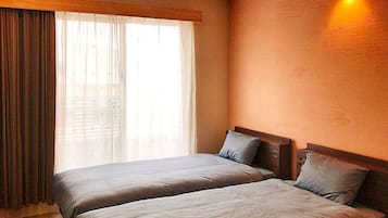 Habitación de hotel con dos camas, un ventanal con cortinas y una lámpara fijada a la pared.