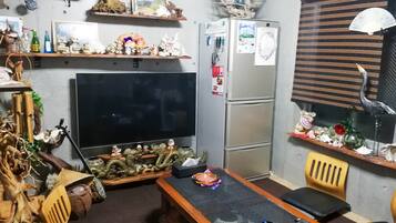 A compact living space with a flat-screen TV, a refrigerator, and a dining table with chairs.