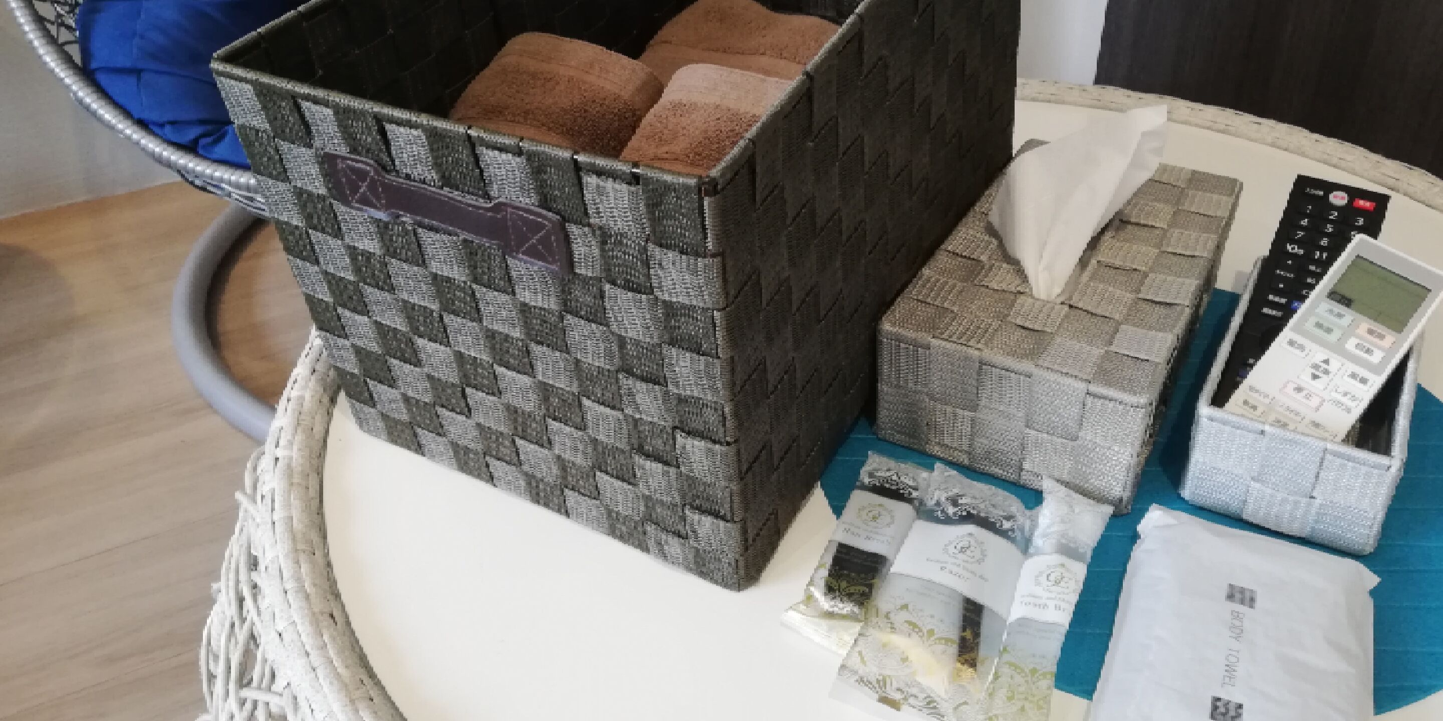 A basket containing various items including a woven basket, a tissue box, a remote control, and some packaged goods.
