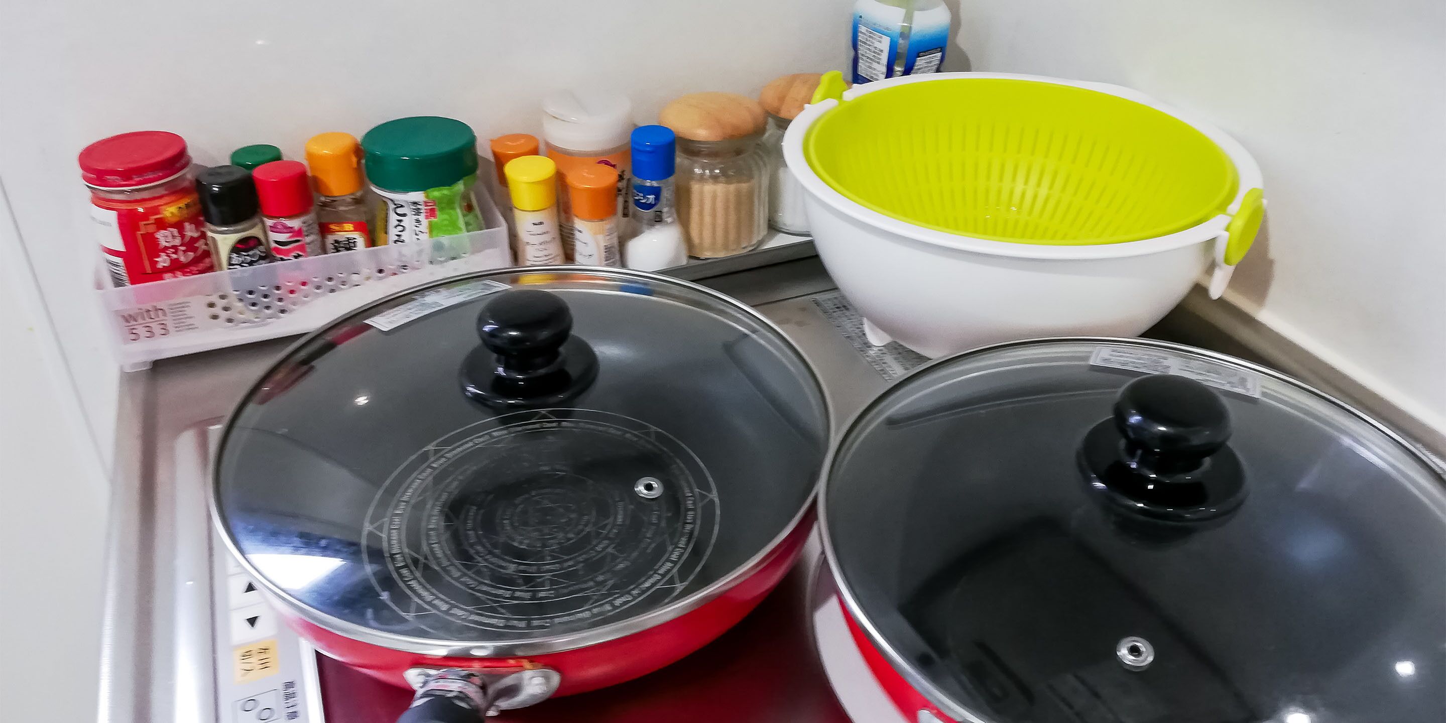 Un plan de travail de cuisine avec deux casseroles rouges, une passoire blanche et divers condiments.