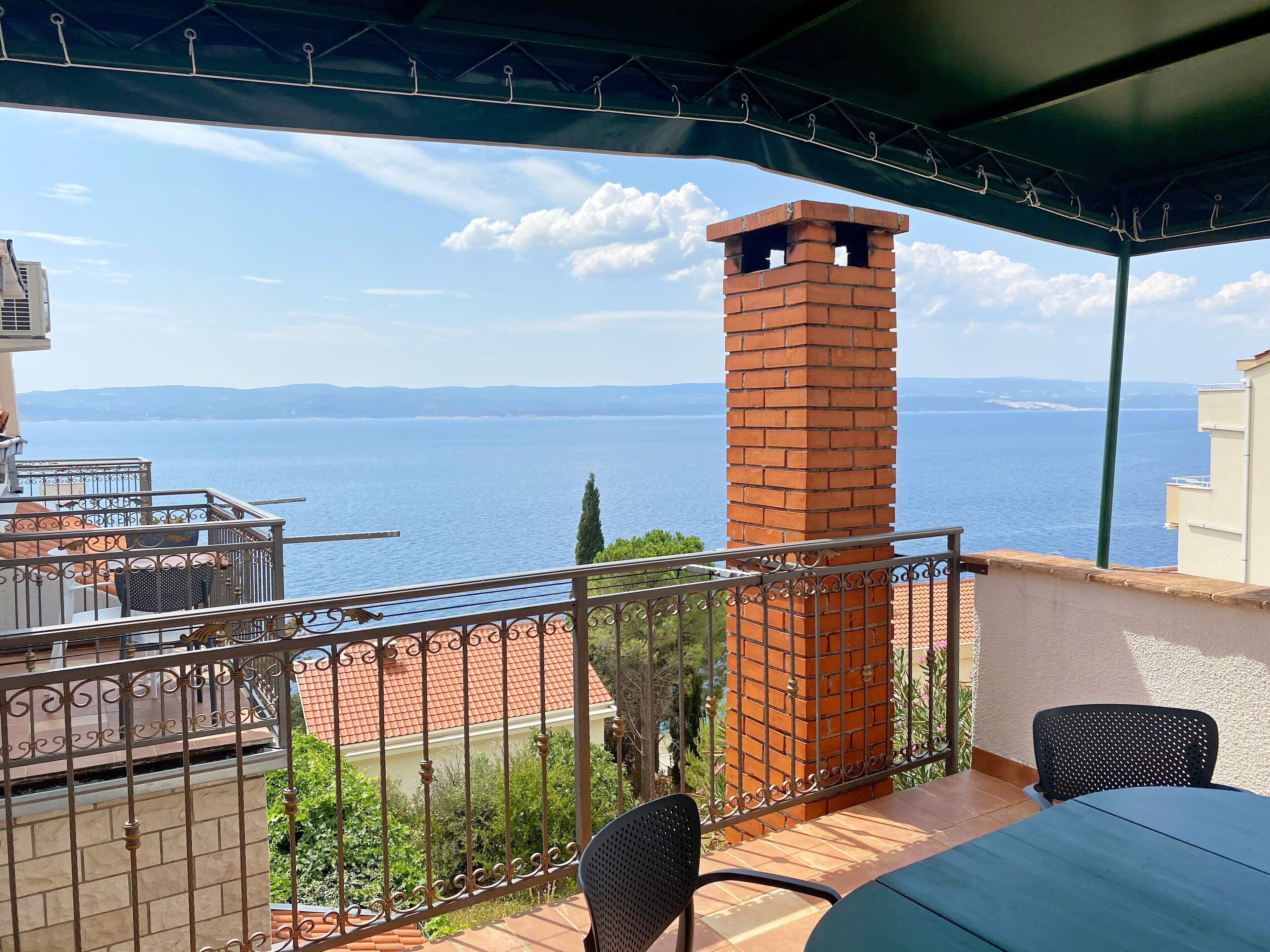 A balcony with a view of the sea, a brick chimney, and outdoor furniture.