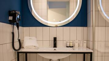 Un baño con lavamanos blanco, un espejo con luz, una toalla y artículos de aseo.