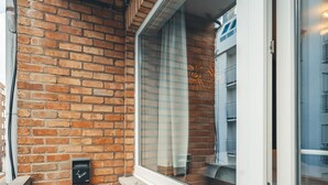 A small, enclosed balcony with a brick wall, a window with a curtain, and a door. - Prado Next Door (Ostend)
