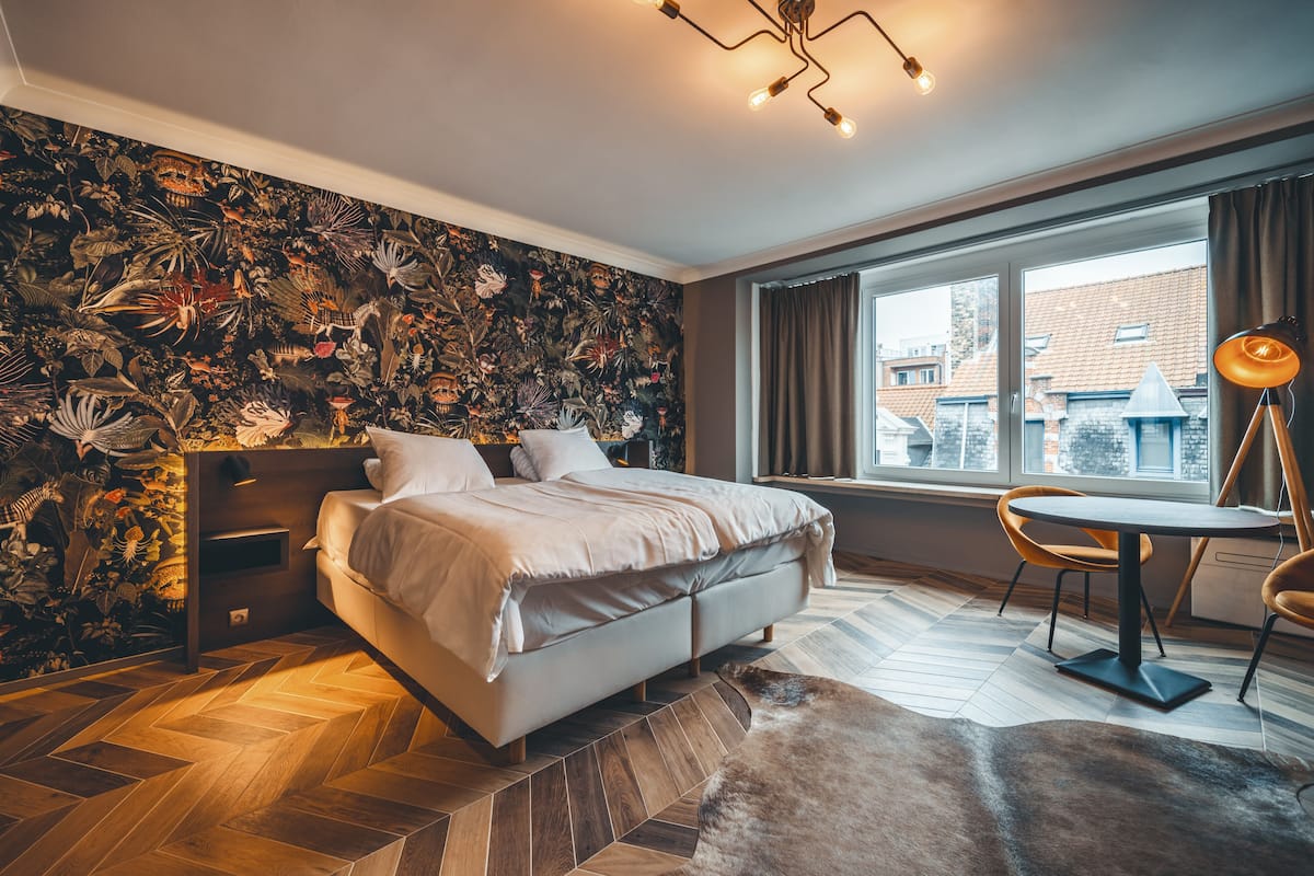 Un dormitorio moderno con una cama grande, una zona de comedor con mesa y sillas, y vistas de la ciudad a través de amplios ventanales.
