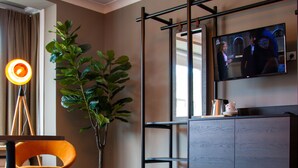 A modern room with a herringbone wood floor, a leather sofa, a potted plant, a television mounted on the wall, and a wooden cabinet. - Prado Next Door (Ostend)