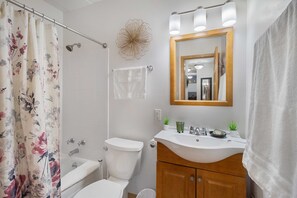 Un baño con cortina de ducha, inodoro, lavabo con espejo y toallero.