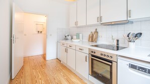 Een moderne keuken met witte kastjes, een houten vloer, een inbouwoven en een vaatwasser.