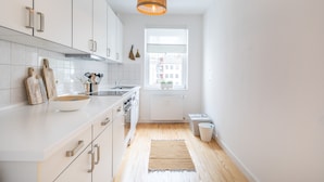Een moderne keuken met witte kasten, een houten aanrecht, een groot raam en een hangende lamp.