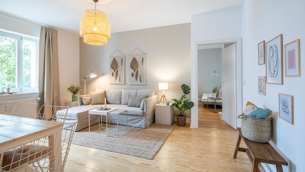 Een moderne woonkamer met een bank, eettafel en stoelen. Er is een lamp, een kamerplant en kunstwerken aan de muren.