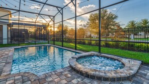 Une piscine avec un jacuzzi, entourée d’une terrasse en briques et d’une clôture en métal.