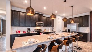 Une cuisine moderne avec des meubles de couleur bois foncé, des appareils en acier inoxydable et un îlot central doté de tabourets de bar.