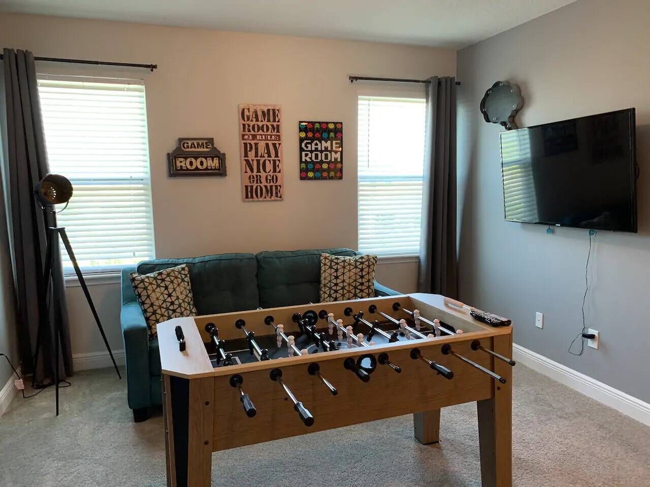 A room with a foosball table, a sofa, and a television mounted on the wall.