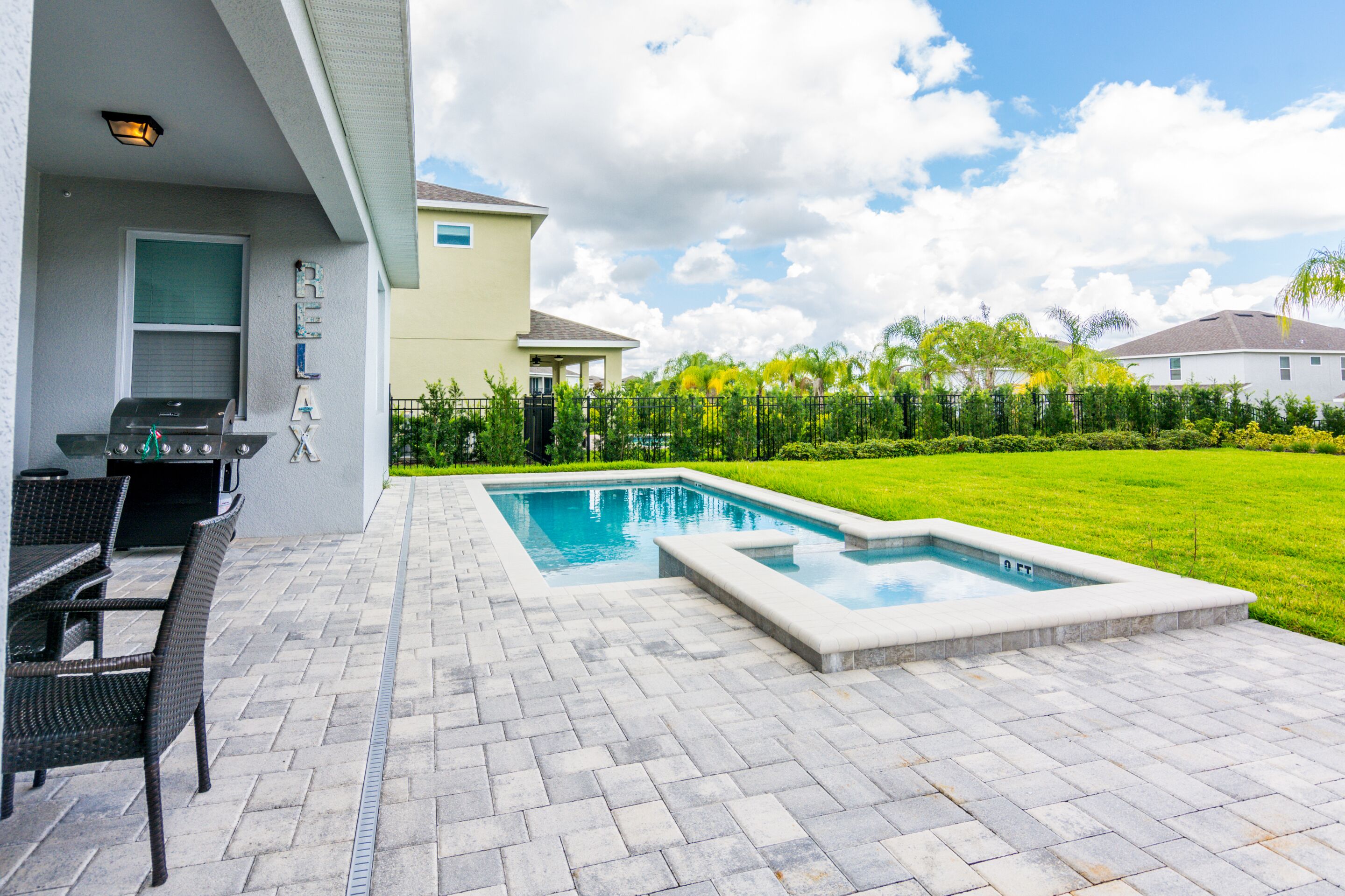 A backyard with a swimming pool, a barbecue grill, and a patio area with chairs.