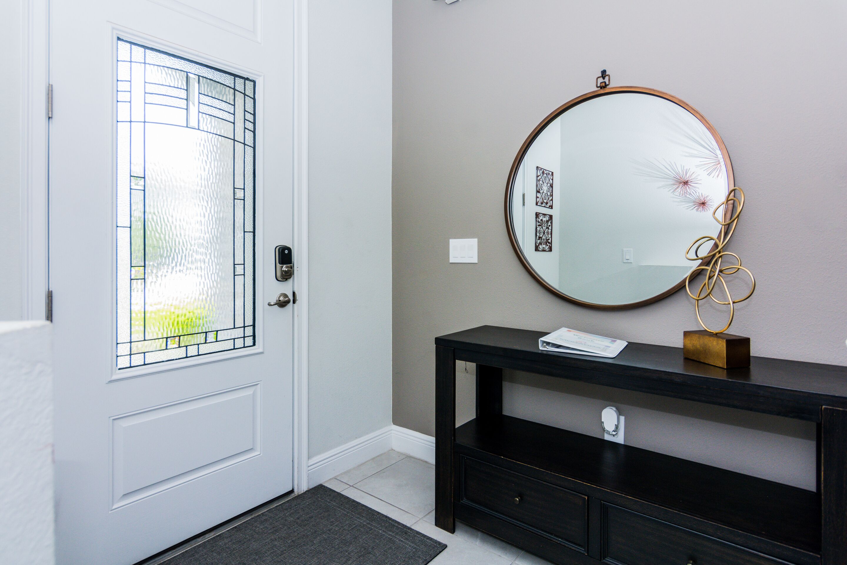 A hallway with a white door, a dark wooden console table, and a round mirror with a gold frame.