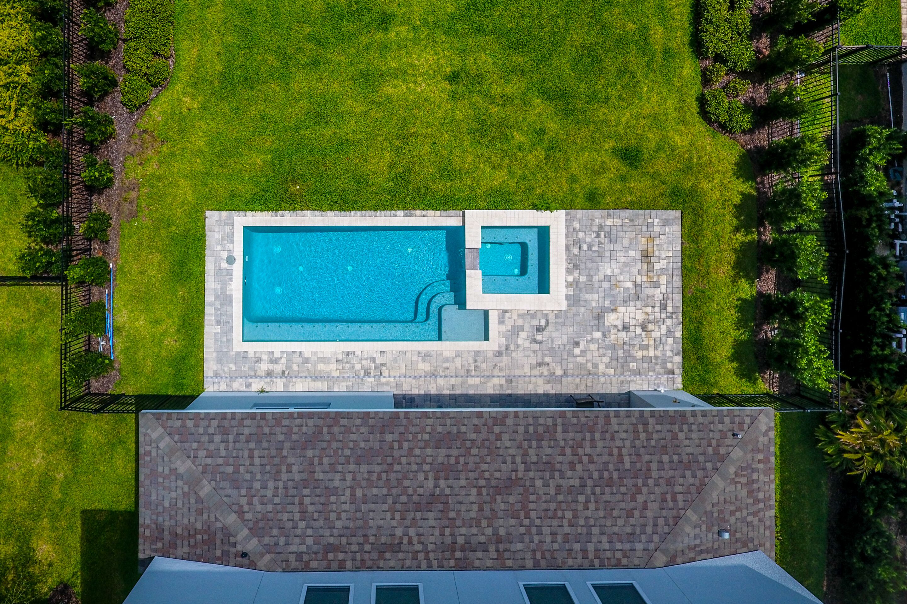Vue aérienne d’une propriété dotée d’une piscine, d’un petit bassin adjacent et d’une terrasse en briques.