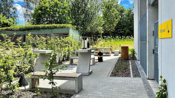 Un patio con mesas al aire libre, un edificio con techo verde y un cartel que dice 
