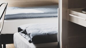Una habitación de hotel moderna con una cama, una silla, una mesita y un cubo de basura.