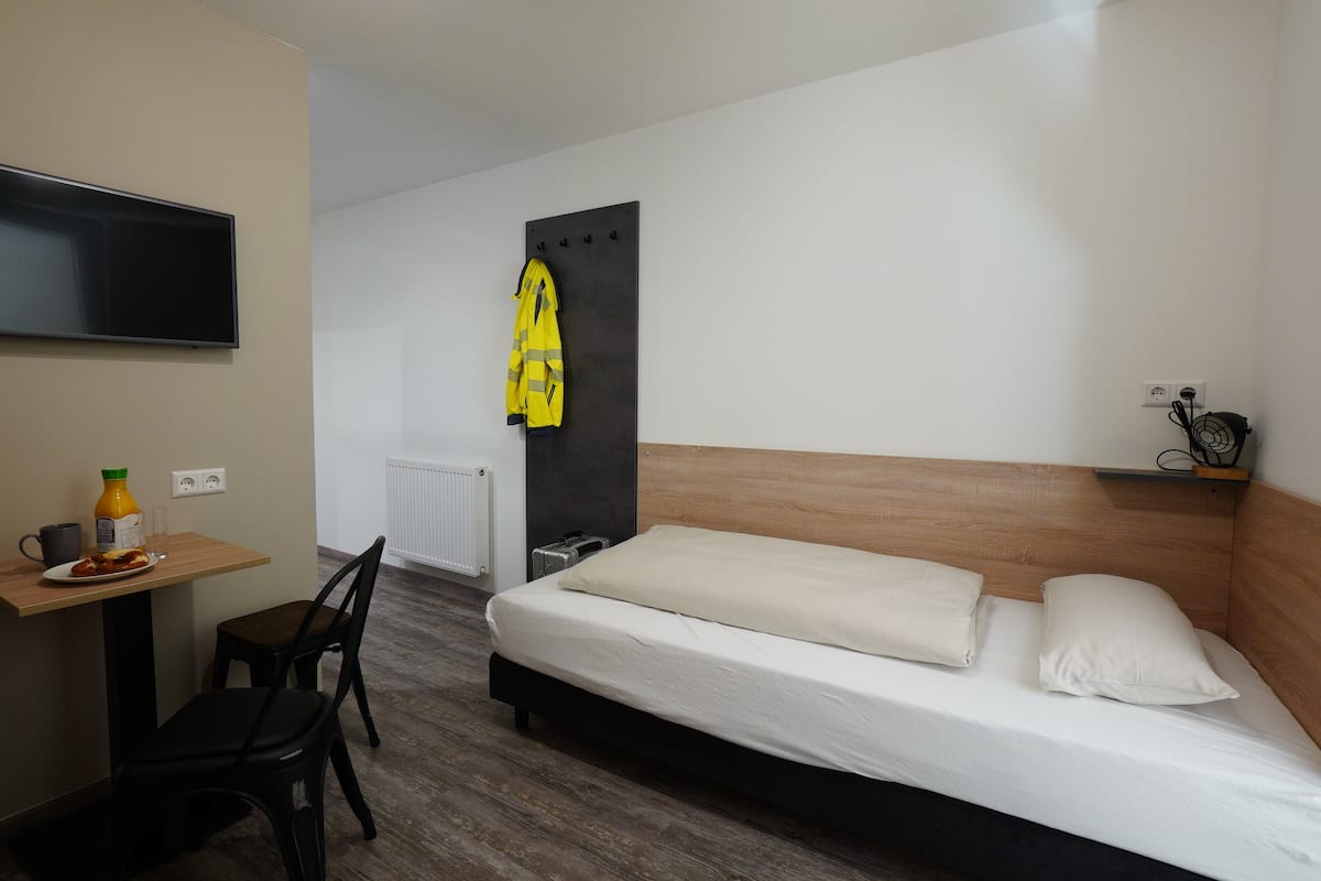 Une chambre d’hôtel avec un lit, un bureau et une chaise, un téléviseur fixé au mur et un manteau accroché à un crochet.