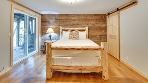A bedroom with a wooden bed frame, a nightstand with a lamp, and a sliding door leading to a balcony. - Raven Rock - 31 Acres, HOT TUB, Stream, fire Pit, Private, High Speed Internet (Henderson County)