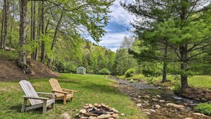A campsite with two Adirondack chairs, a fire pit, a small shed, and a stream. - Raven Rock - 31 Acres, HOT TUB, Stream, fire Pit, Private, High Speed Internet (Henderson County)