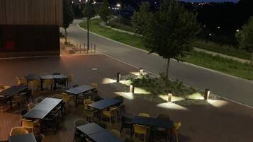 An outdoor seating area with tables and chairs, a flower bed, and a building with a 'HOTEL' sign.