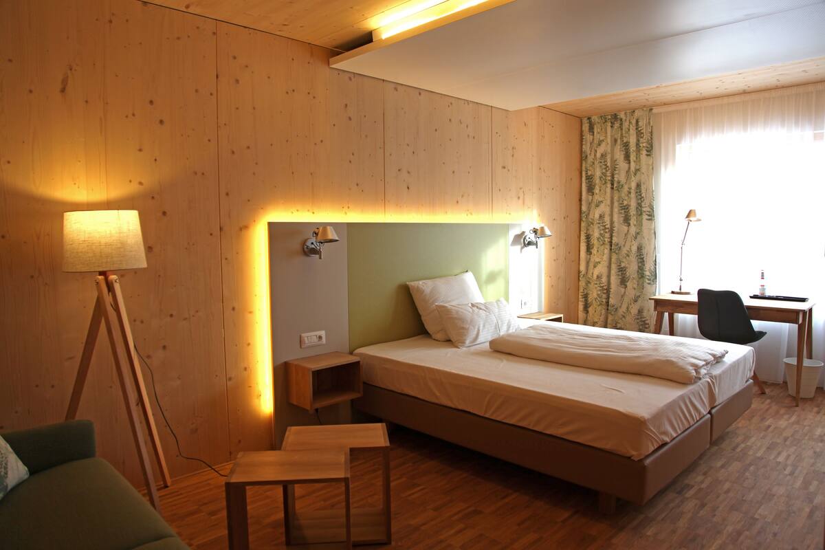Ein Hotelzimmer mit Holzboden, einem Bett mit grünem Kopfteil, einem Schreibtisch mit Stuhl und einer Lampe.