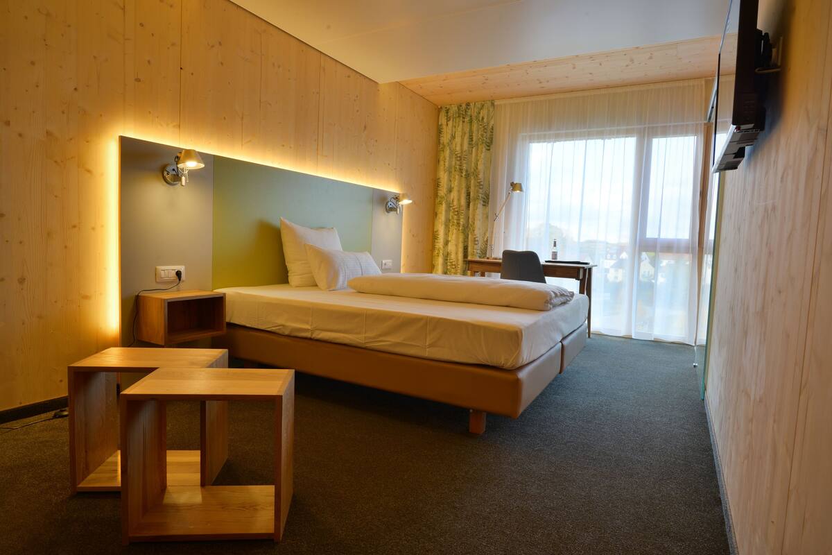 Ein Hotelzimmer mit Bett, Nachttischen, einem Schreibtisch und Blick ins Freie.