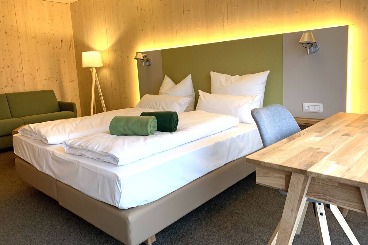 Ein Hotelzimmer mit einem großen Bett, einem grünen Sofa, einem Holztisch und einer Lampe.