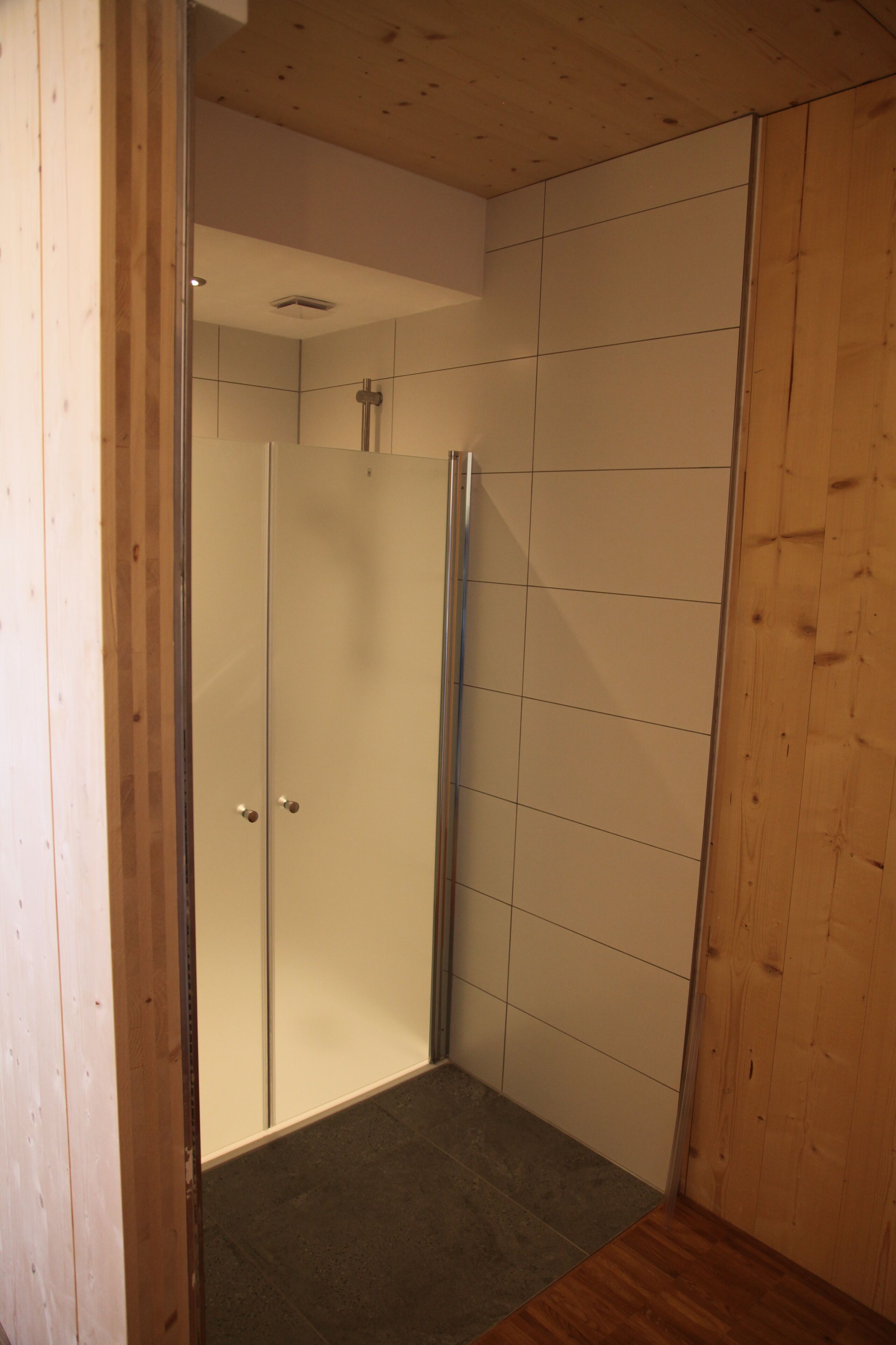 Un área de ducha con puerta de vidrio, paredes de madera y suelo de baldosas.