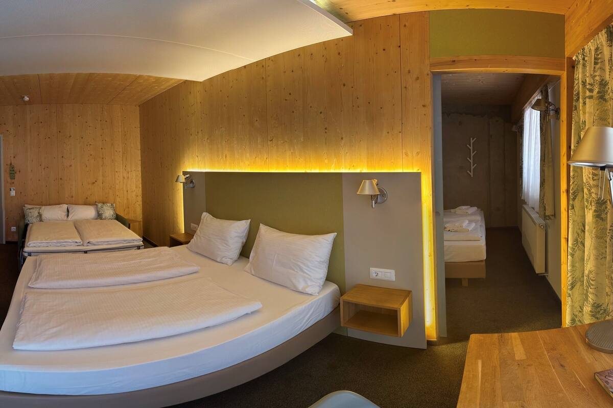 Ein Zimmer mit einem großen Bett, einem Nachttisch, einer Lampe und einem kleinen Holzregal.