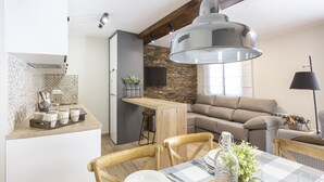 Une cuisine moderne avec un mur recouvert de pierres apparentes, des poutres en bois au plafond et un coin repas agrémenté d’une nappe à carreaux.