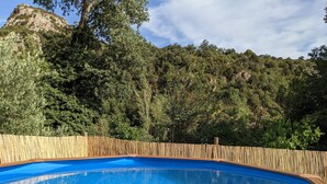 Une piscine d’un bleu éclatant, entourée d’une clôture en bois, avec une colline boisée en arrière-plan.