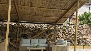 Un espace extérieur aménagé, abrité et doté de mobilier en osier, avec un mur en pierre en arrière-plan.