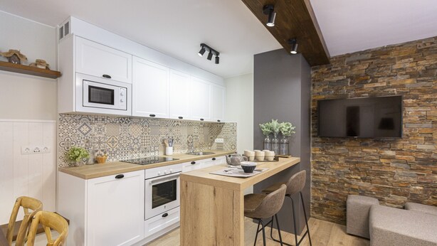 Une cuisine moderne avec des armoires blanches, un comptoir en bois et un pare-feu en pierre. On y trouve également un coin bar avec des tabourets et un téléviseur à écran plat fixé à un mur en pierre.