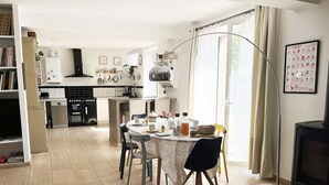 Cozinha moderna com área de jantar, destacando uma mesa redonda, cadeiras e uma grande janela com cortinas.