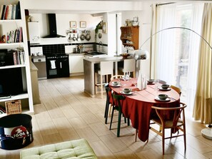 A modern kitchen with a dining area, featuring a round table set for four, a built-in oven, and a variety of kitchen utensils displayed on the wall.
