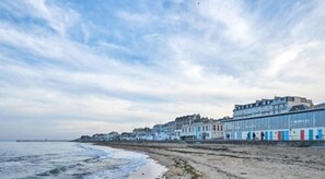 A coastal hotel with a long beachfront, a pier extending into the sea, and a row of colorful buildings along the shore.