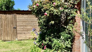 Um jardim com cerca de madeira, muro de tijolos e planta em vaso com flores cor-de-rosa.