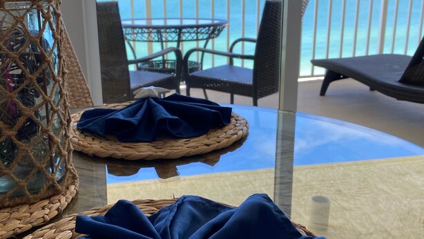 A glass table with woven baskets and a starfish decoration on a balcony overlooking the sea.