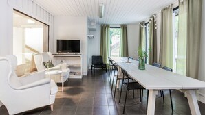A modern living room with a white sofa, a dining table, and a TV.