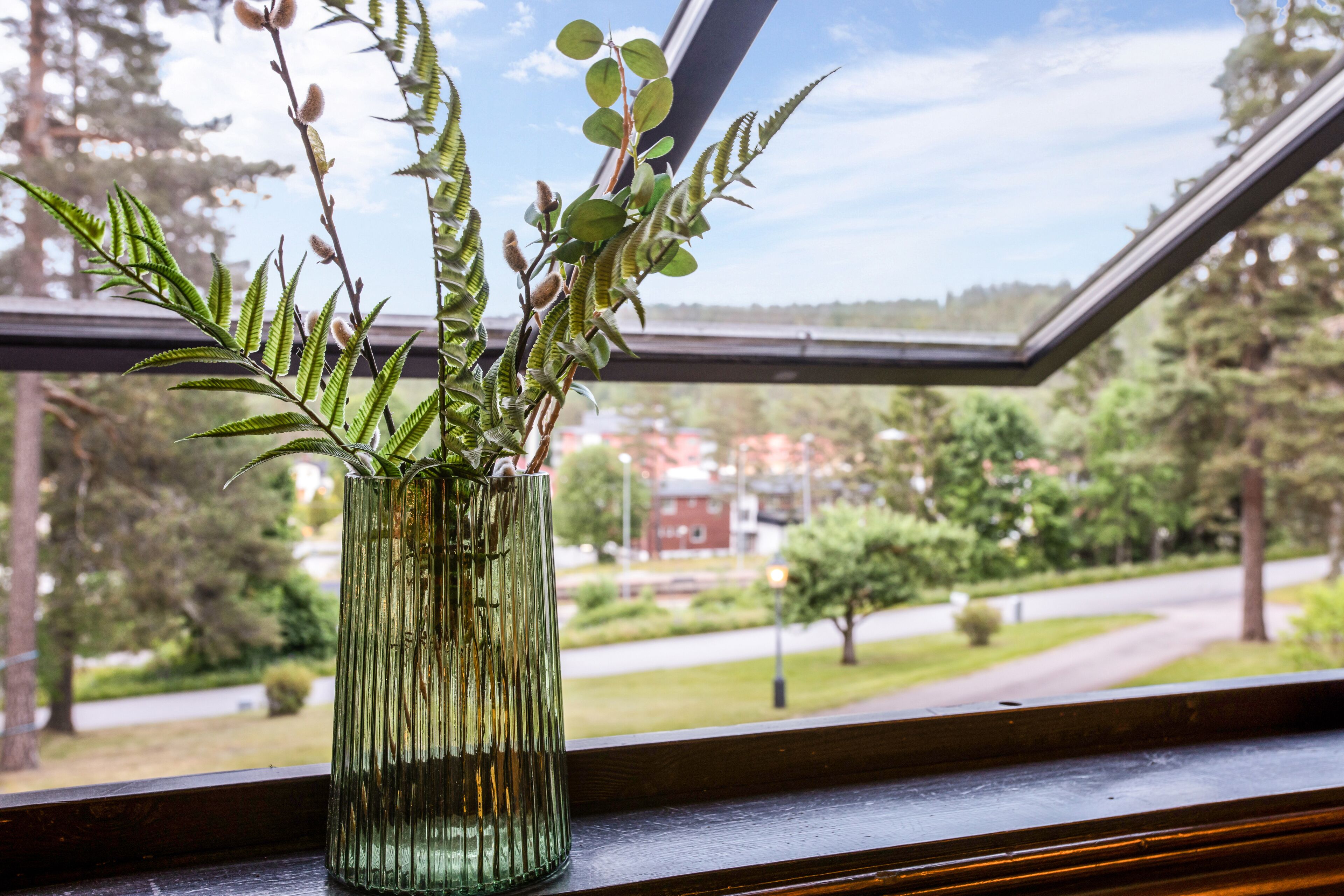 A green glass vase with a plant on a windowsill.