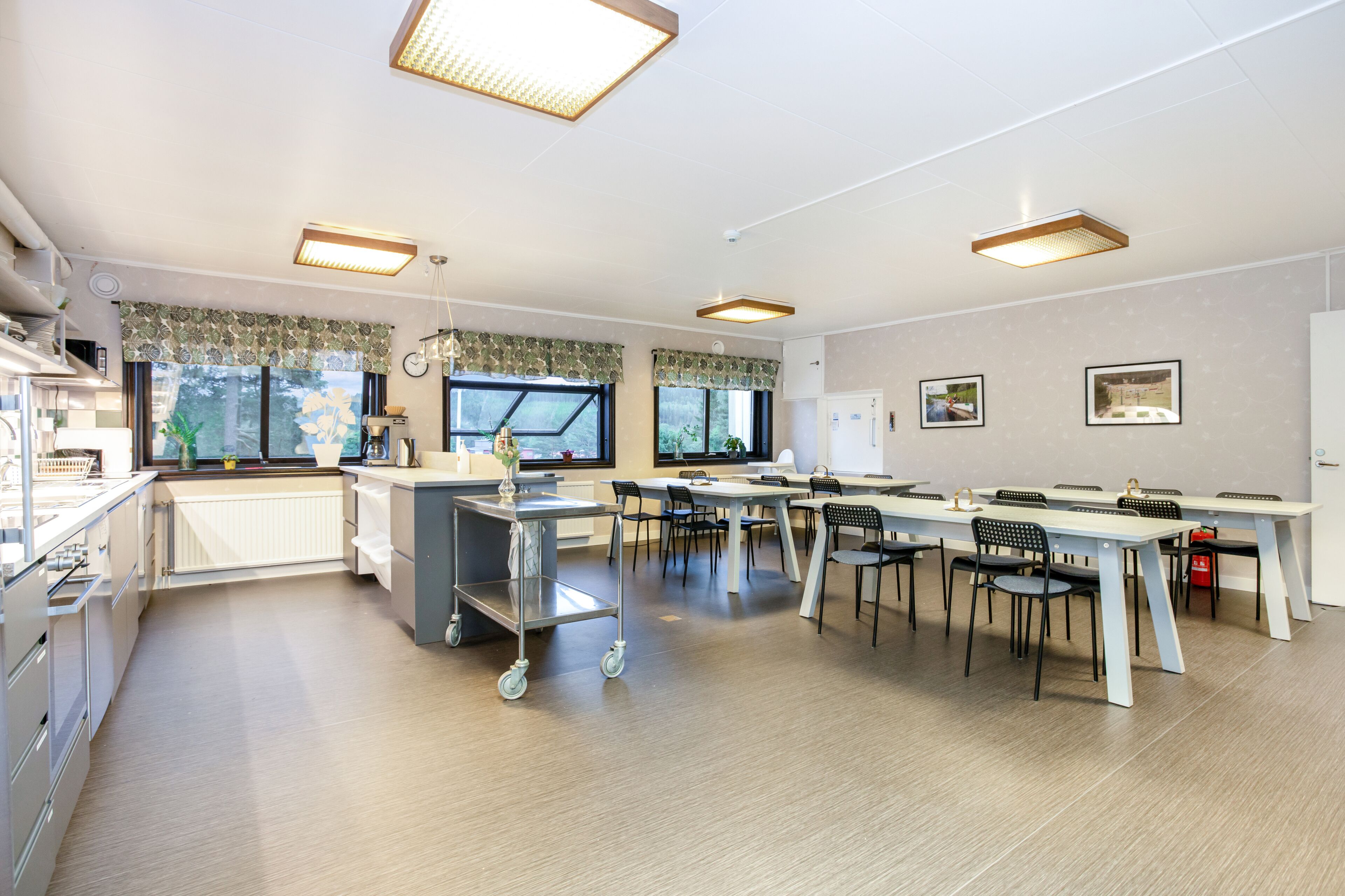 Een moderne keuken met een centraal eiland, grote ramen en een eethoek met tafels en stoelen.