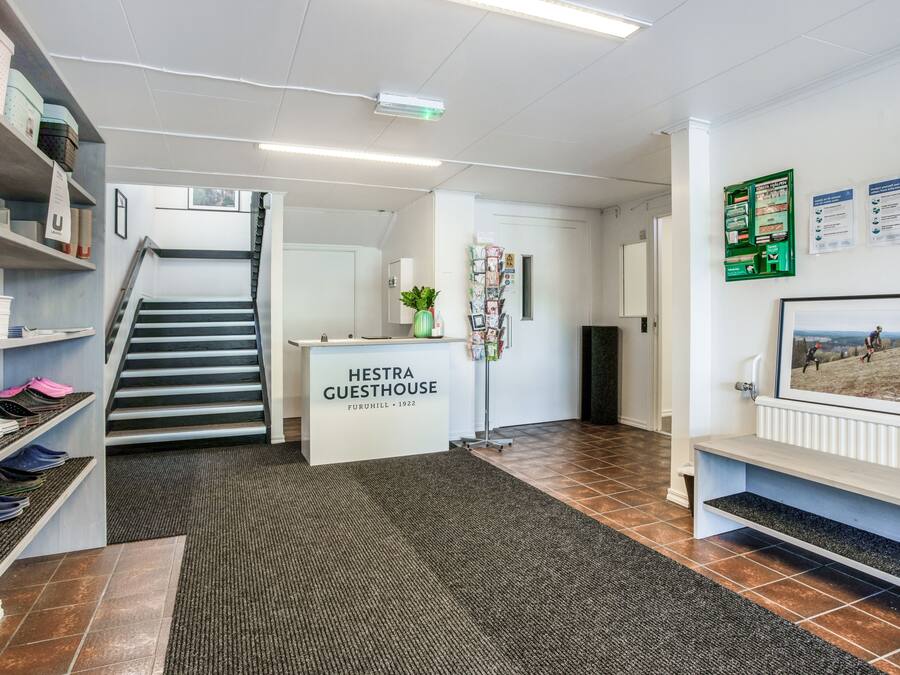 Un espace d’accueil avec un escalier, un comptoir de réception portant l’inscription « Hestra Guesthouse » et un panneau d’affichage contenant des informations.